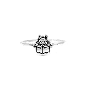 May include: A silver ring with a cat peeking out of a box design.
