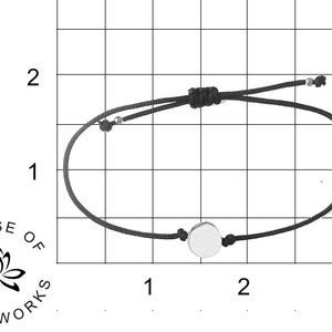 May include: A black string bracelet with a silver circle charm. The bracelet is approximately 3 inches in diameter.