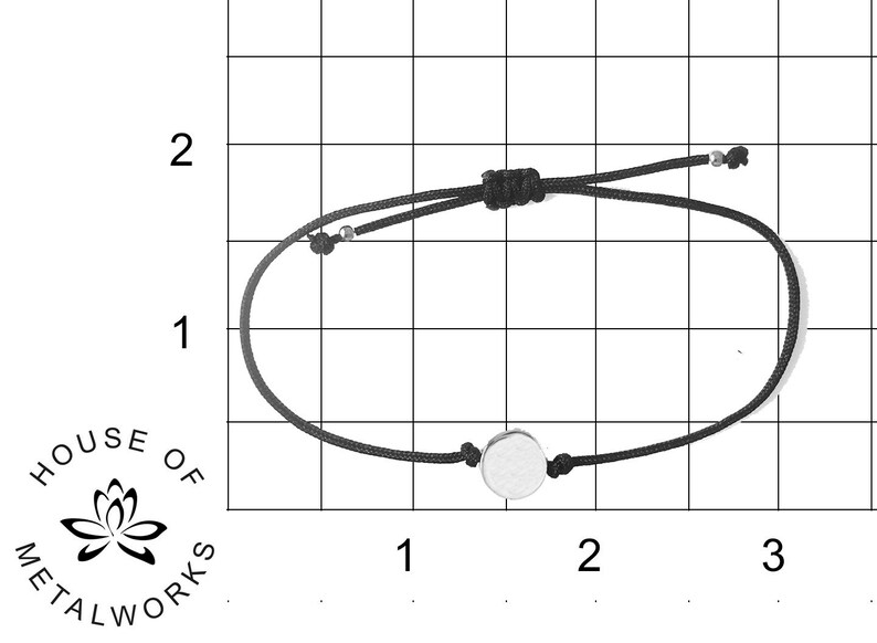 May include: A black string bracelet with a silver circle charm. The bracelet is approximately 3 inches in diameter.