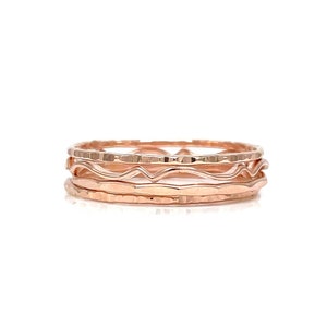 May include: Set of four rose gold stacking rings. The rings are thin and delicate, with a hammered texture and a wavy design.