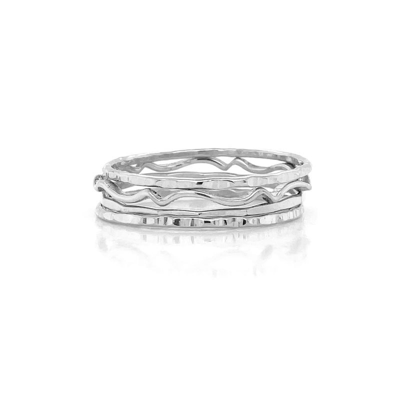 May include: Set of four silver stacking rings with different textured finishes. The rings are all thin and delicate, and they are designed to be worn together.
