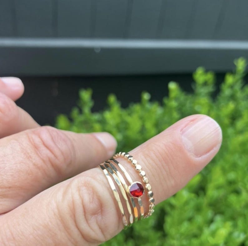 May include: A set of four gold rings, one with a red gemstone, worn on a finger.