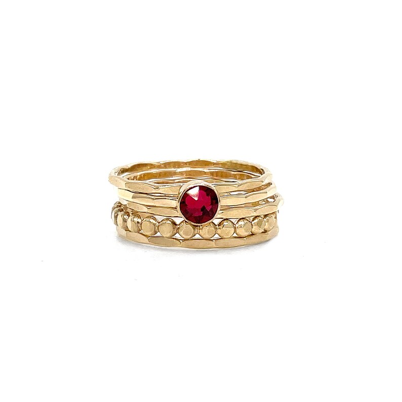 May include: A set of four gold rings with a red gemstone in the centre. The rings are stacked on top of each other and have a hammered texture.