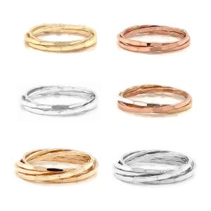 K&ouml;nnte beinhalten: Auswahl an ineinandergreifenden Ringen in Gold, Ros&eacute;gold und Silber. Jeder Ring hat eine strukturierte, geh&auml;mmerten Oberfl&auml;che. Die Ringe sind in verschiedenen Anordnungen angeordnet, um ihre Design- und Farbvariationen zu zeigen.