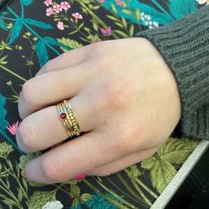 May include: A set of four gold stacking rings with a single red gemstone on the middle ring.