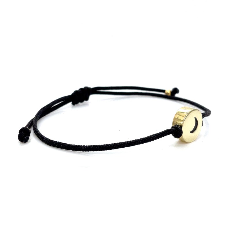 May include: A black string bracelet with a gold charm featuring a crescent moon design.