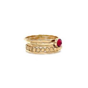 May include: A set of four gold rings, one with a red gemstone, stacked on a white background.