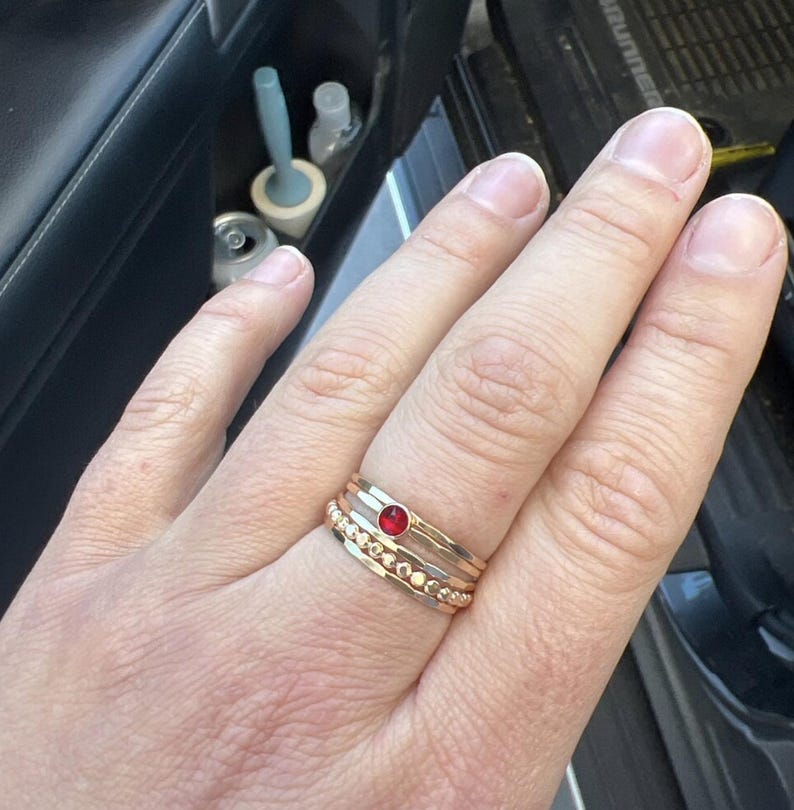 May include: A hand wearing a set of four gold rings. The top ring has a red gemstone.