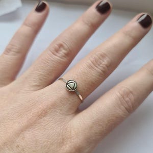 May include: A silver ring with a small, round, white-colored design featuring a triangle inside a circle.