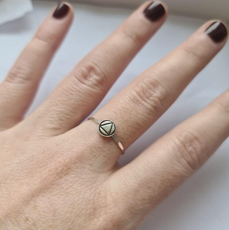 May include: A silver ring with a small, round, white-colored design featuring a triangle inside a circle.