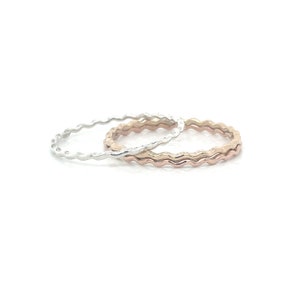 May include: Two thin wavy rings, one silver and one rose gold, stacked on top of each other.