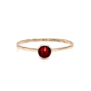 May include: A simple gold band ring with a single red gemstone in the center.