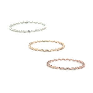 May include: Three thin wavy rings in silver, gold, and rose gold.