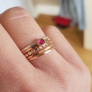 May include: A set of four gold rings with a single red gemstone in the centre. The rings are stacked on top of each other and have a hammered texture.