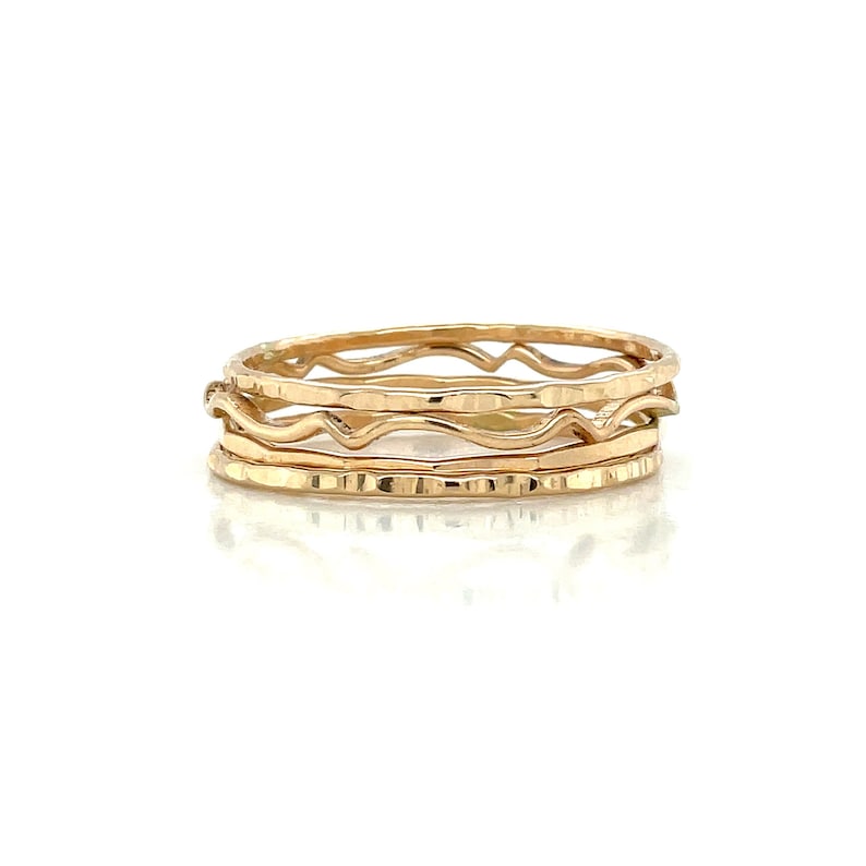 May include: Set of four gold-toned stacking rings. The rings are thin and have a hammered texture. The top ring has a wavy design.