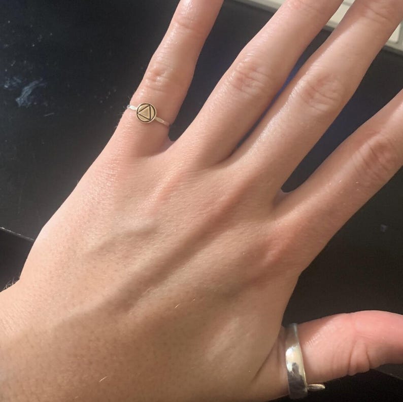 May include: A silver ring with a small, round, gold-colored charm featuring a triangle symbol.