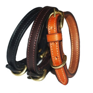 Puede incluir: Tres collares de perro de cuero en negro, marrón y naranja. El collar naranja tiene una hebilla de latón.