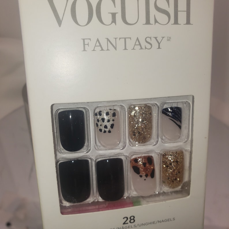 K&ouml;nnte beinhalten: Eine wei&szlig;e Schachtel mit VOGUISH FANTASY-Press-on-N&auml;geln. Die N&auml;gel sind schwarz, goldglitzernd und im Leopardenmuster. Die Schachtel enth&auml;lt 28 N&auml;gel. Auf der Oberseite der Schachtel steht der Markenname in silbernen Buchstaben.