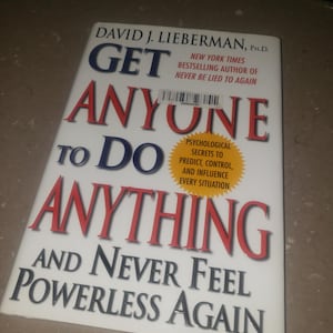 May include: A book titled "Get Anyone to Do Anything" by David J. Lieberman, Ph.D. The cover is white with bold blue and red text. It promises psychological secrets to predict, control, and influence every situation.