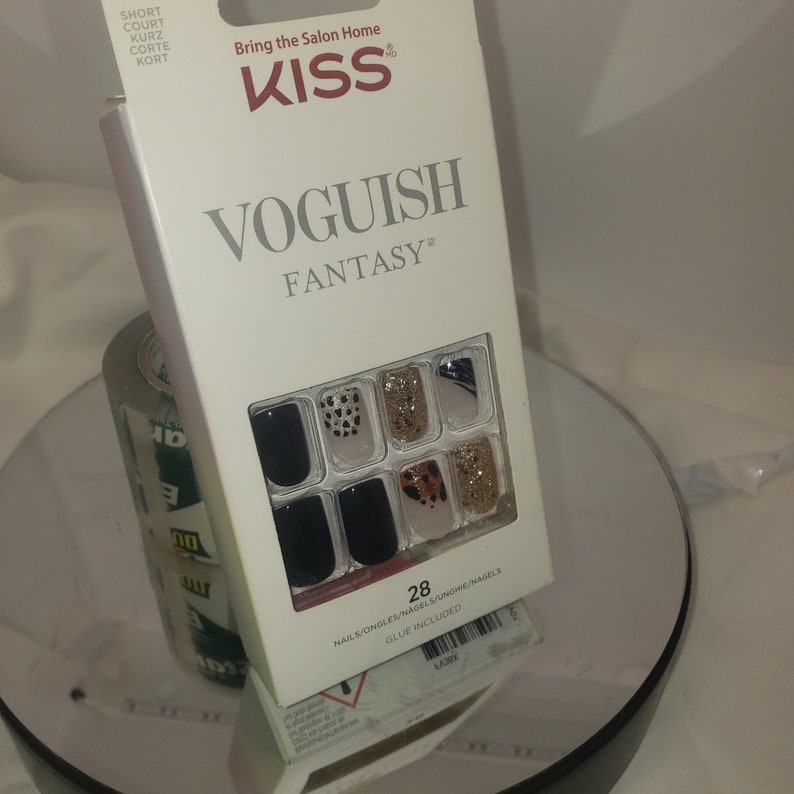 K&ouml;nnte beinhalten: Eine wei&szlig;e Schachtel mit KISS Voguish Fantasy Kunstn&auml;geln. Die Schachtel tr&auml;gt den Text "Bring the Salon Home" und "KISS". Die N&auml;gel sind schwarz, goldglitzernd und im Leopardenmuster. Die Schachtel enth&auml;lt auch den Text "28 NAILS/ONGLES/NAGELS/UNGHE/NAGELS GLUE INCLUDED".
