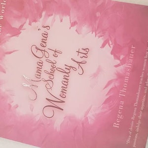 May include: A pink book cover with a floral design and the title "Mama Gena's School of Womanly Arts" in a dark pink font. The author's name, "Regena Thomashauer", is printed below the title in a smaller font.