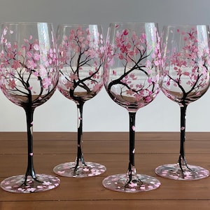 May include: Set of four clear glass wine glasses with hand-painted pink cherry blossom trees and black stems.