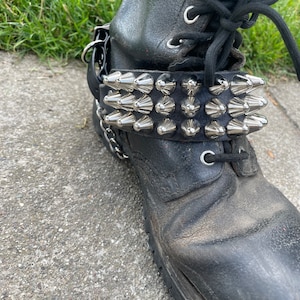 May include: Black leather boots with a silver studded strap around the ankle.
