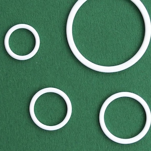 May include: Five white plastic rings of different sizes on a green background.