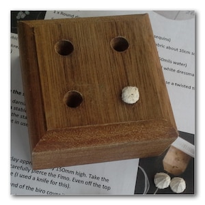 May include: A wooden block with four holes and a white bead in one of the holes. The block is sitting on a white piece of paper with text.