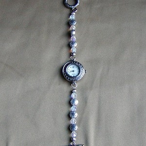 May include: A silver watch with a white face and a beaded chain. The chain has clear and light purple beads.