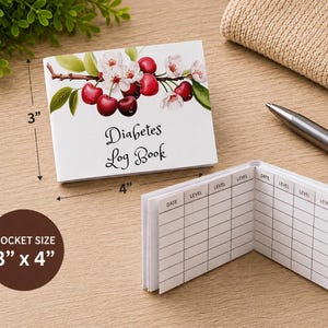 May include: A white pocket-sized diabetes log book measuring 3 inches by 4 inches. The cover features a cherry blossom and fruit illustration with the text Diabetes Log Book. The interior pages contain a grid with columns labeled Date and Level.