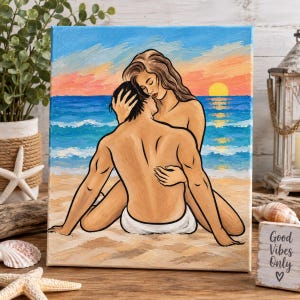 Peut inclure: Une peinture sur toile représentant deux silhouettes s'enlaçant sur une plage de sable au coucher du soleil. La scène montre un océan bleu avec des vagues à crête blanche, un soleil doré à l'horizon et un ciel aux teintes orange et bleu.