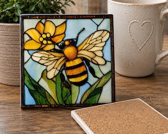 May include: A square coaster featuring a stained glass style design of a yellow and black bee perched on a yellow flower with green leaves against a light blue background. The coaster has a dark frame and a cork backing for a non-slip surface.