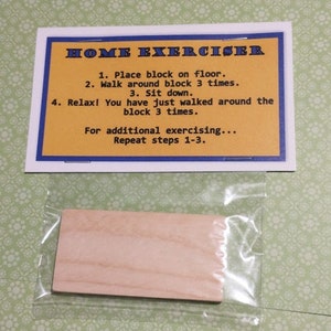 May include: A rectangular wooden block enclosed in a clear plastic bag, accompanied by a white card with a blue border and yellow center. The card features the text: HOME EXERCISER, 1. Place block on floor. 2. Walk around block 3 times. 3. Sit down.