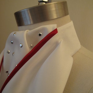 May include: White dress shirt with a red ribbon trim and silver embellishments. The shirt is folded and displayed on a mannequin.