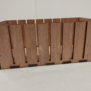 May include: A rectangular wooden crate with a brown stain finish and black trim. The crate has vertical slats and is empty.