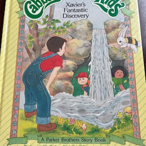 May include: A vintage Cabbage Patch Kids storybook, "Xavier's Fantastic Discovery." The cover shows a boy in denim overalls, a waterfall, and other children. A rabbit with a striped back is also visible. Published by Parker Brothers.