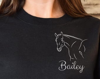 May include: Black sweatshirt featuring a white outline of a horse's head and neck. The name "Bailey" is written in cursive below the horse graphic. The sweatshirt has long sleeves and a crew neck.