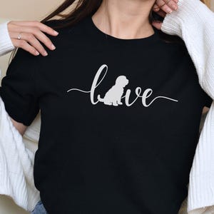 May include: Black crew neck t-shirt with the word "love" in cursive script and a white silhouette of a dog. The shirt is made of a soft material.