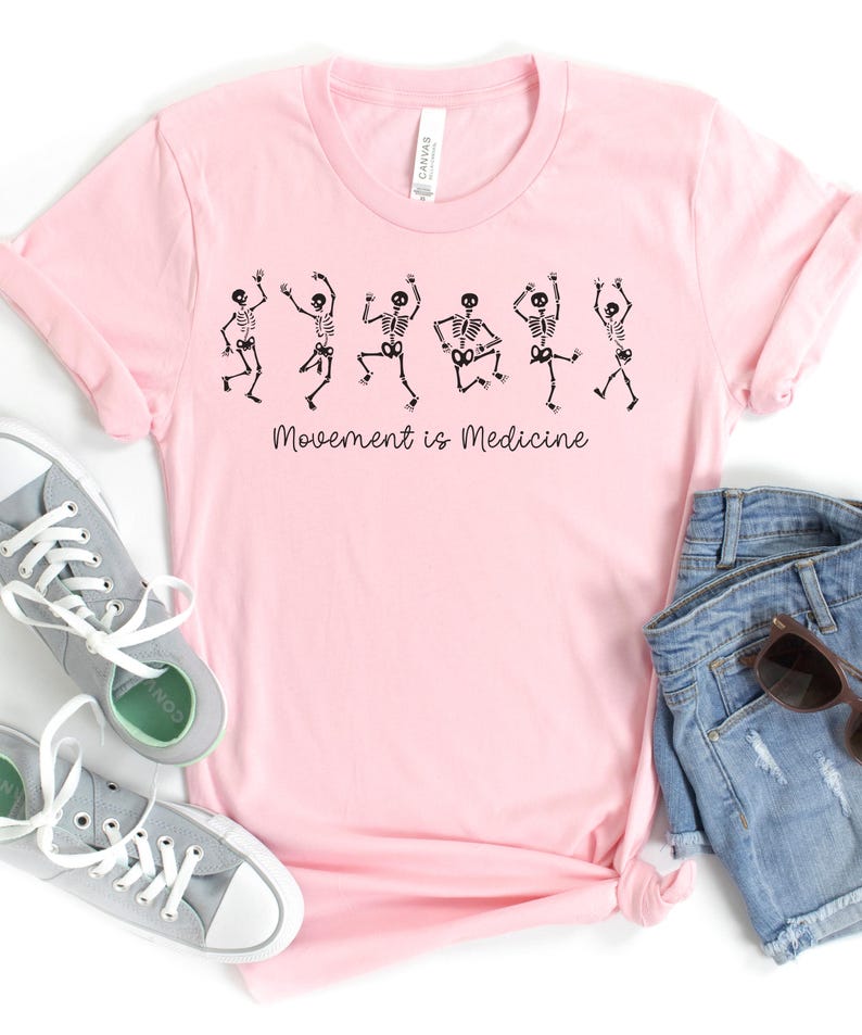 K&ouml;nnte beinhalten: Rosa T-Shirt mit einer Grafik von tanzenden Skeletten und dem Text "Bewegung ist Medizin".