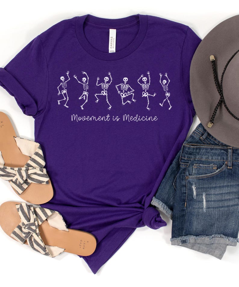 K&ouml;nnte beinhalten: Lilafarbenes T-Shirt mit einer wei&szlig;en Grafik von tanzenden Skeletten und dem Text "Bewegung ist Medizin".