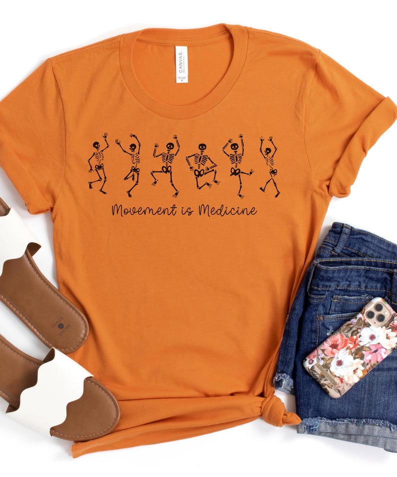 K&ouml;nnte beinhalten: Orangefarbenes T-Shirt mit einer schwarzen Grafik von tanzenden Skeletten und dem Text "Bewegung ist Medizin".