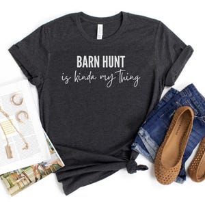 May include: Dark gray t-shirt with the text "Barn Hunt is kinda my thing" in white lettering.