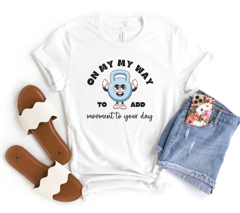 Puede incluir: Camiseta blanca con un personaje de pesa rusa de dibujos animados y el texto "ON MY WAY TO ADD movement to your day." La camiseta se combina con pantalones cortos de mezclilla, un tel&eacute;fono y sandalias marrones con correas blancas con volantes.