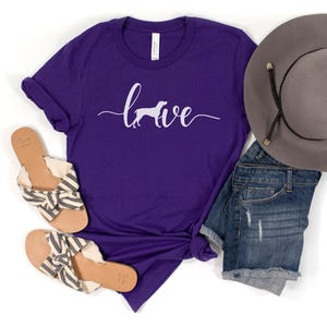 May include: Purple t-shirt with the word "love" written in cursive with a white silhouette of a dog in the "o".