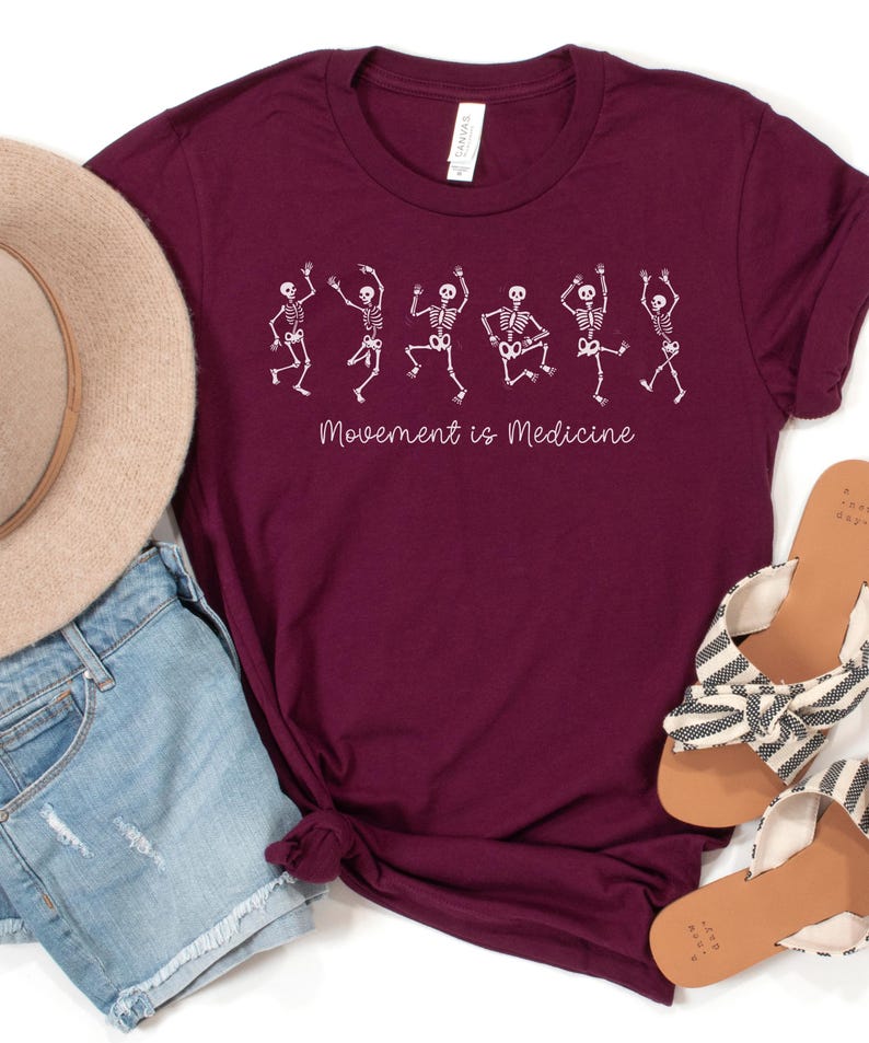 K&ouml;nnte beinhalten: Burgunderfarbenes T-Shirt mit einer wei&szlig;en Grafik von tanzenden Skeletten und dem Text "Bewegung ist Medizin".