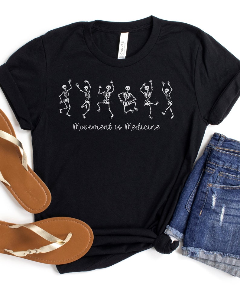 K&ouml;nnte beinhalten: Schwarzes T-Shirt mit einer wei&szlig;en Grafik von tanzenden Skeletten und dem Text "Bewegung ist Medizin".