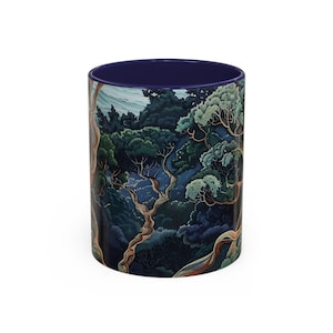 Op de afbeelding: Een keramische mok met een donkerblauwe rand en een kleurrijke illustratie van een bos scène met bomen en takken. De illustratie is in tinten groen, blauw en bruin.