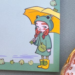 May include: A girl wearing a green frog raincoat and yellow rain boots holds a yellow umbrella. She has red hair in braids and is carrying a green frog purse. Green frogs are falling from the sky.