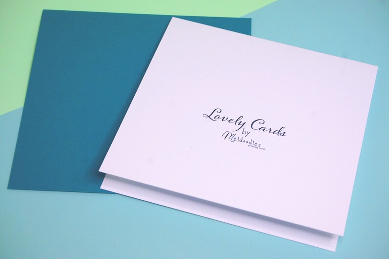 Puede incluir: Una tarjeta blanca con el texto "Lovely Cards by Meldoodles" impreso en tinta negra. La tarjeta est&aacute; sobre una superficie azul claro.